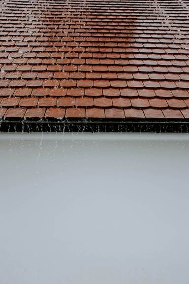 Close-up of a tiled roof and gutter during rainfall, illustrating roof repair in California