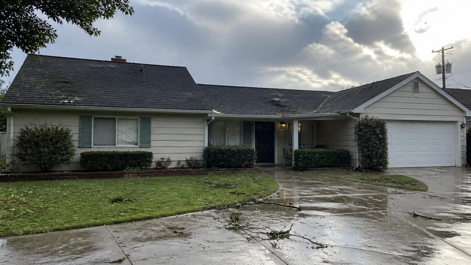 Clovis home after a storm with wind-damaged shingles and branches scattered across the roof and yard